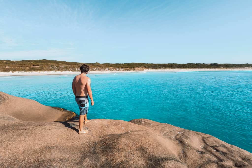 Man standing on top of the twilight beach boulder, in Esperance WA, preparing to jump from it into the turquoise waters