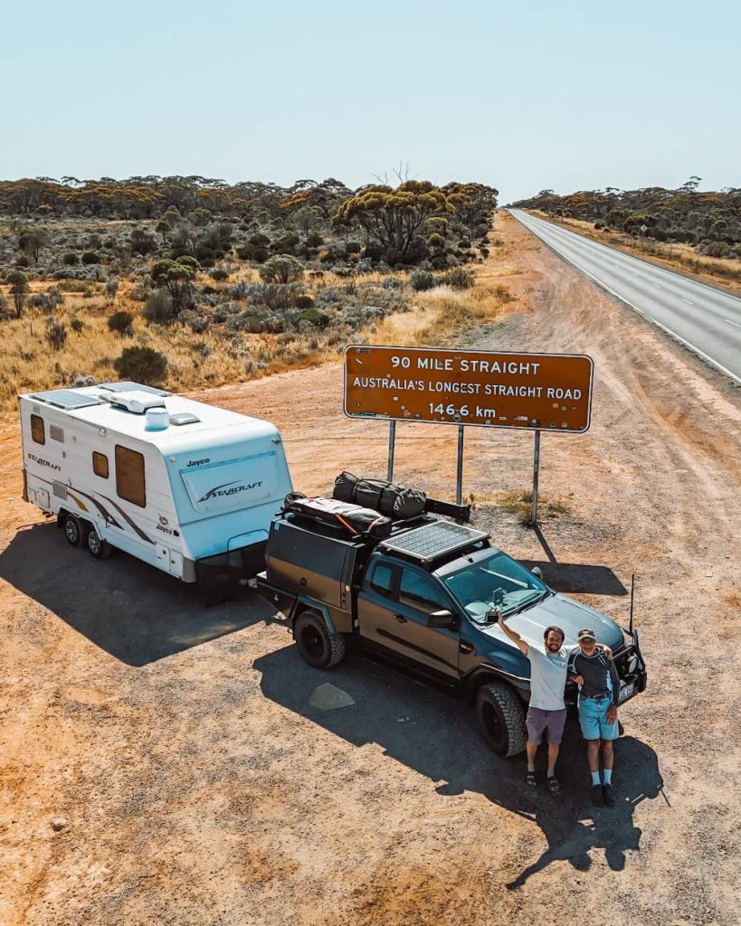 Two men standing in front of a 4WD at the 90 mile straight sign in the nullarbor, western australia