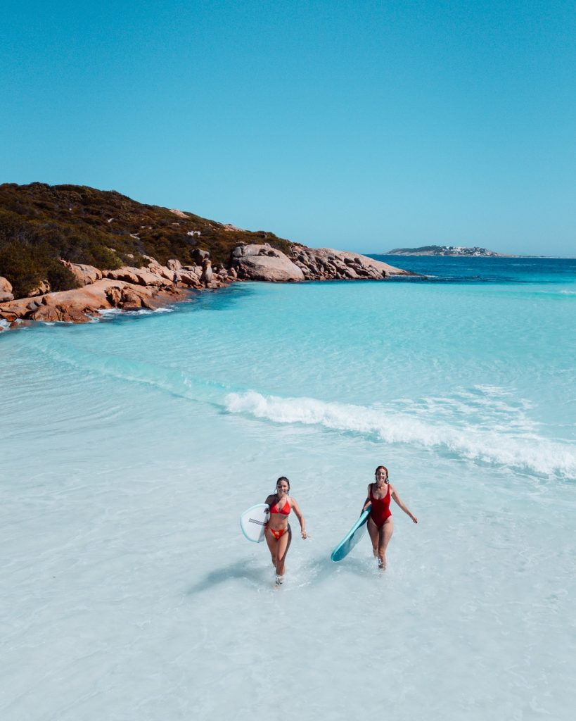 two women with surfboards walking out of the waters of wharton beach in esperance, western australia