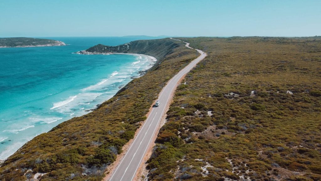 A drone shot of a winding coastal road near Esperance, Western Australia, with turquoise waters on one side and bushland on the other, ideal for scenic road trips in Australia.