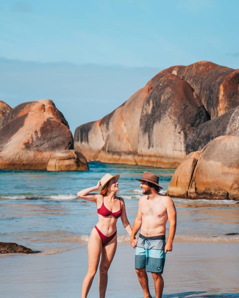 A couple walks hand-in-hand in front of the massive granite formations of Elephant Rocks in Denmark, a popular stop on the Perth to Bremer Bay road trip.