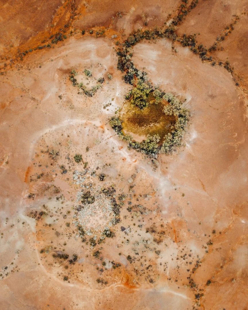 Aerial shot of the Henbury Meteor site with patches of green vegetation, a 4WD stop on the red centre way. The natural textures and colours are vividly visible from above.