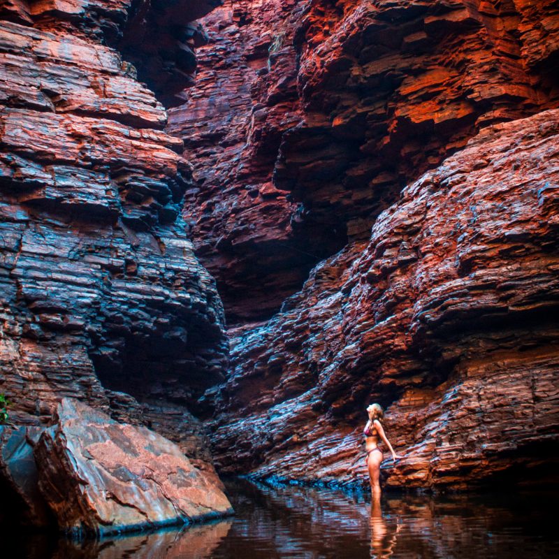 Woman stands in water at Handrail Pool, Weano Gorge, Karijini National Park, surrounded by towering red rock walls.