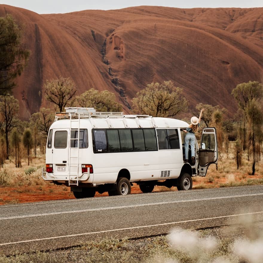 Bec and Chris also known as Salt and Charcoal driving their bus "Bunji" with Uluru in the background.