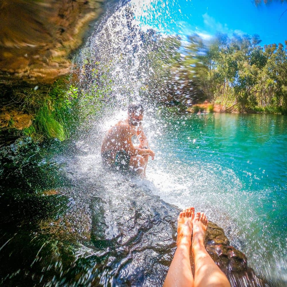 Man sitting underneath gushing waterfall, one of the top ten sites to see in Karijini. This is at the Fern Pool in Karijini, WA.