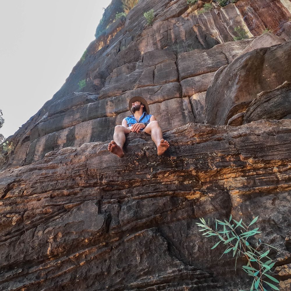 Man sitting, barefoot, on a rock looking out into the sky. If you don't know what to do in Kakadu National Park, this is one of the activities you can do.