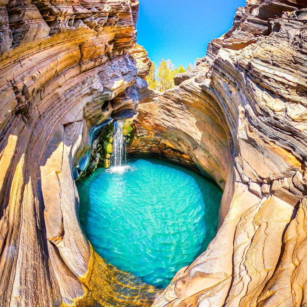 Clear, aqua water body with small waterfall, surrounded by rocks. One of Karijinis finest sites. The Hamersley Gorge in WA.