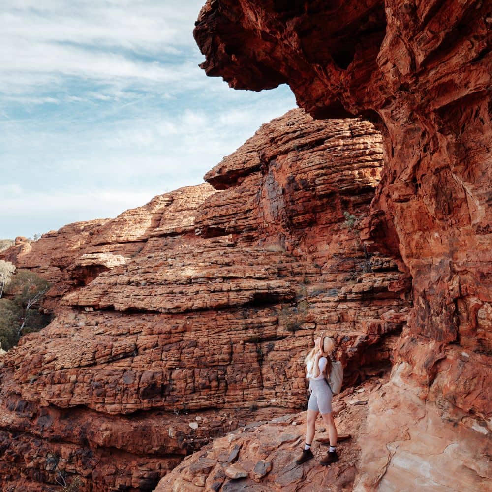 Woman standing on rock looking up into the sky. One of the best parts of hiking in the NT. Found in Alice Springs, in the Northern Territory.