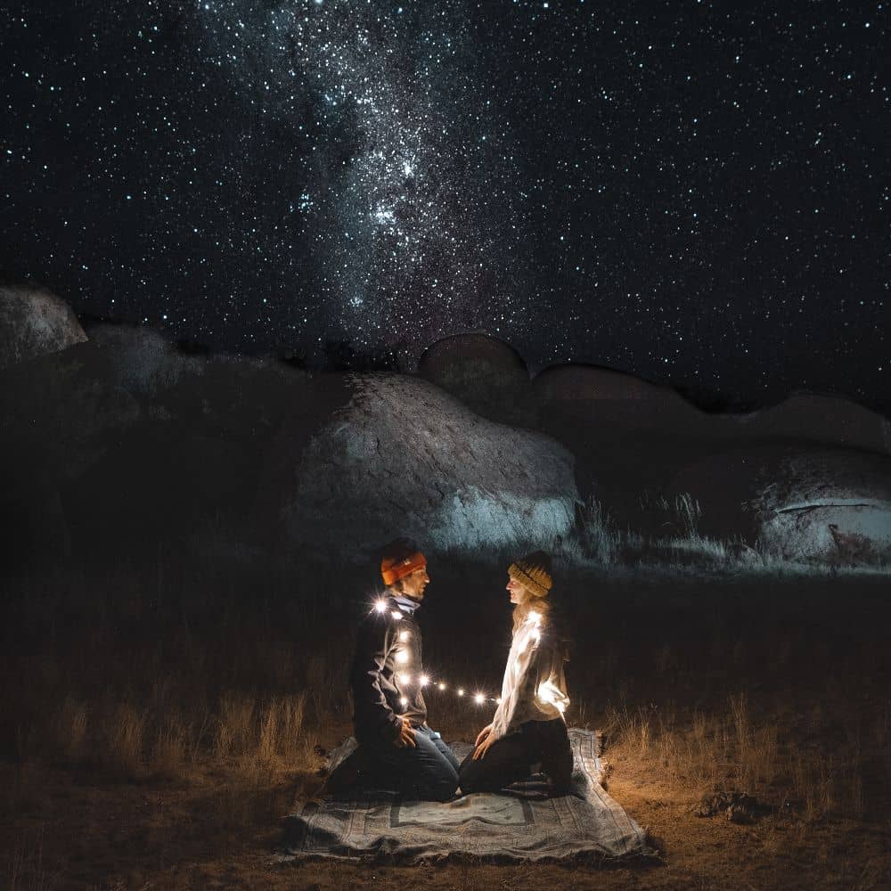 A man and woman staring into one anothers eyes in front of stars and lights. One of the best sites to see in Alice Springs, for no price. This can be found at Alice Springs in the Northern Territory.
