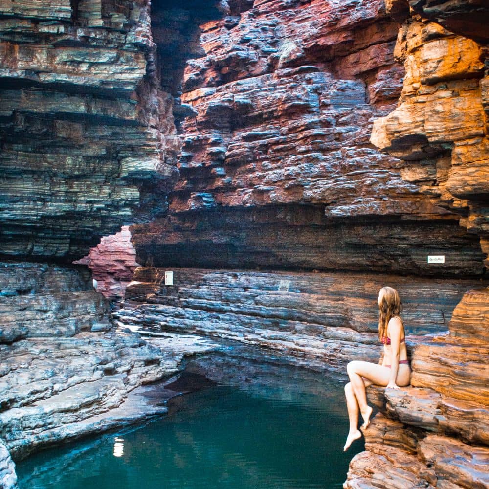 Women sitting on edge of rock overlooking a beautiful water body surrounded by rocks. One of the top ten things to do in Karijini. This is the Kermit's Pool in the Hancock Gorge, Karijini, WA.