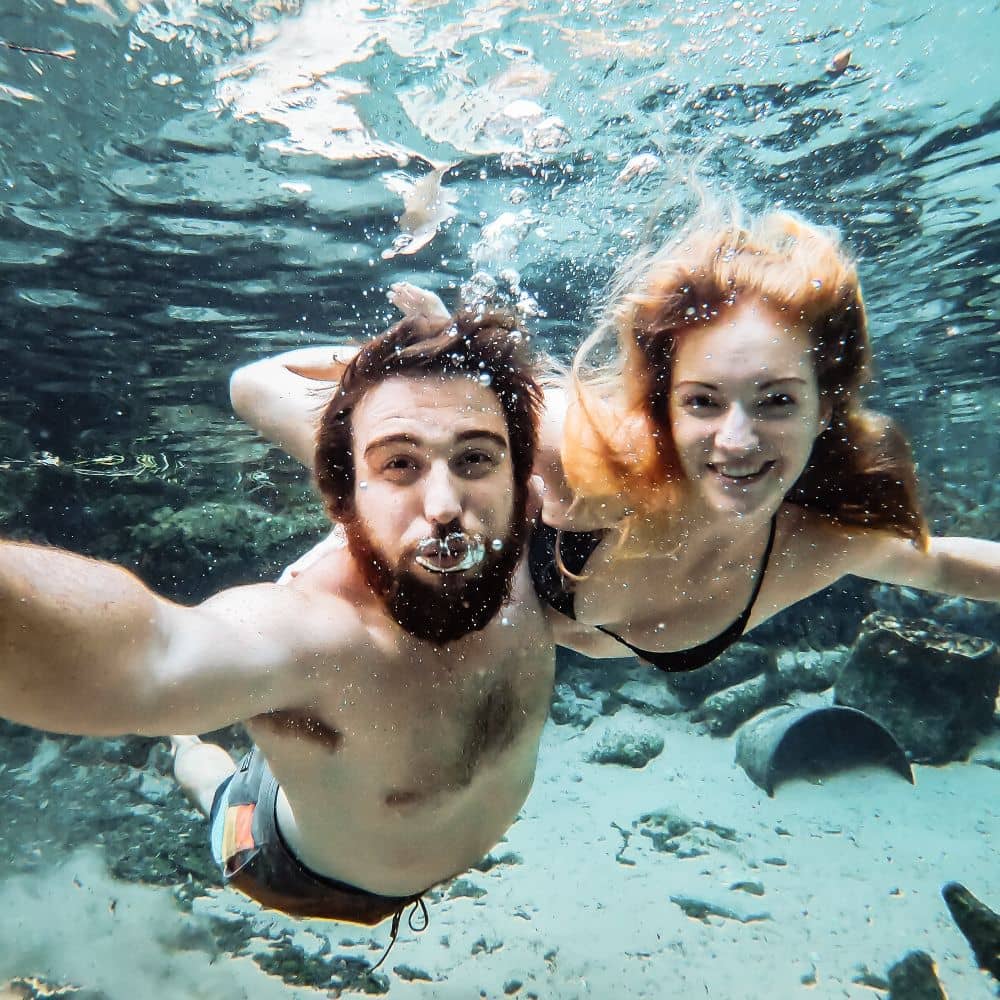 A man and woman smiling whilst taking a selfie underwater. They are at the unforgettable Katherine Hot Springs which some say are able to energize the body. Can be found at the Katherine River.