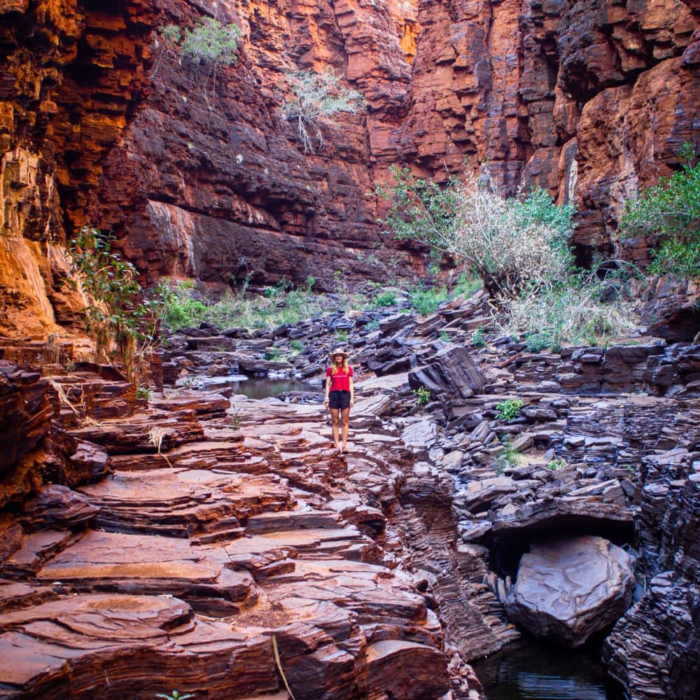 Women standing in middle of rock formation with clear skies above. One of the best sites to see in Karijini. She is standing in the Knox Gorge located in Karijini, Western Australia.
