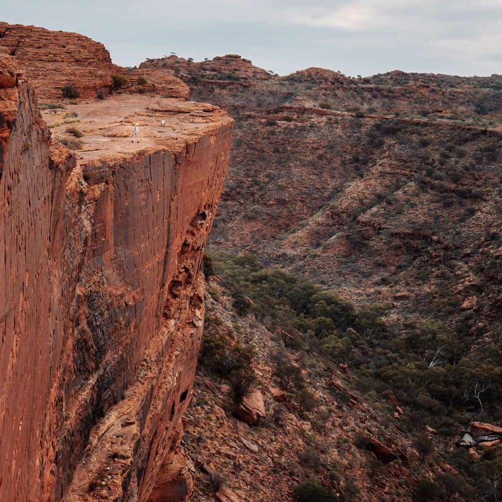 Woman standing on edge of cliff looking out at scenery. What you see when you reach the end of the best hiking trails in the NT. This is found at Kings Canyon, in Alice Springs.