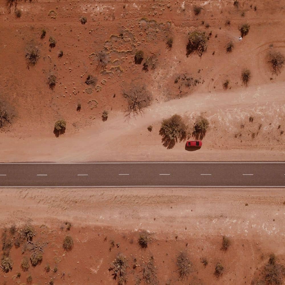 A red car on the side of a desolate road in the middle of the desert. One of the most common places to visit in Alice Springs, Australia's red centre. 