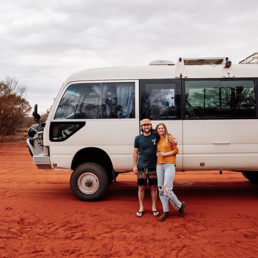 A man and woman standing in front of their van. They know when the best time to go to Uluru for the best experience is. This is camping at Uluru in the Northern Territory.