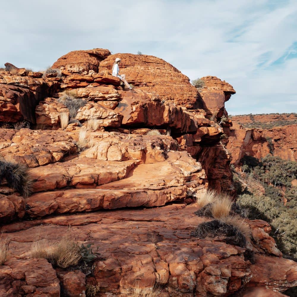 A woman sitting on a rock while looking over at the mountains surrounding her. This is the very best of hiking in the Northern Territory.