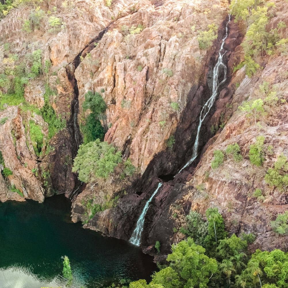 An overtop view of a deep green-blue waterfall rushing down into the water body below, a waterfall many call Litchfield national parks best. This waterfall is Wangi Falls.