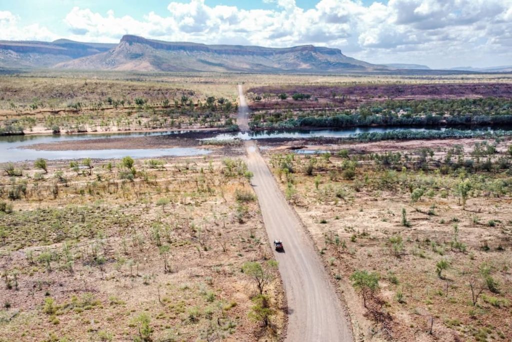 A 4WD approaches the Pentecost River crossing, with mountain ranges rising in the background and the road stretching across the riverbed—one of the most iconic scenes on a gibb river road itinerary.