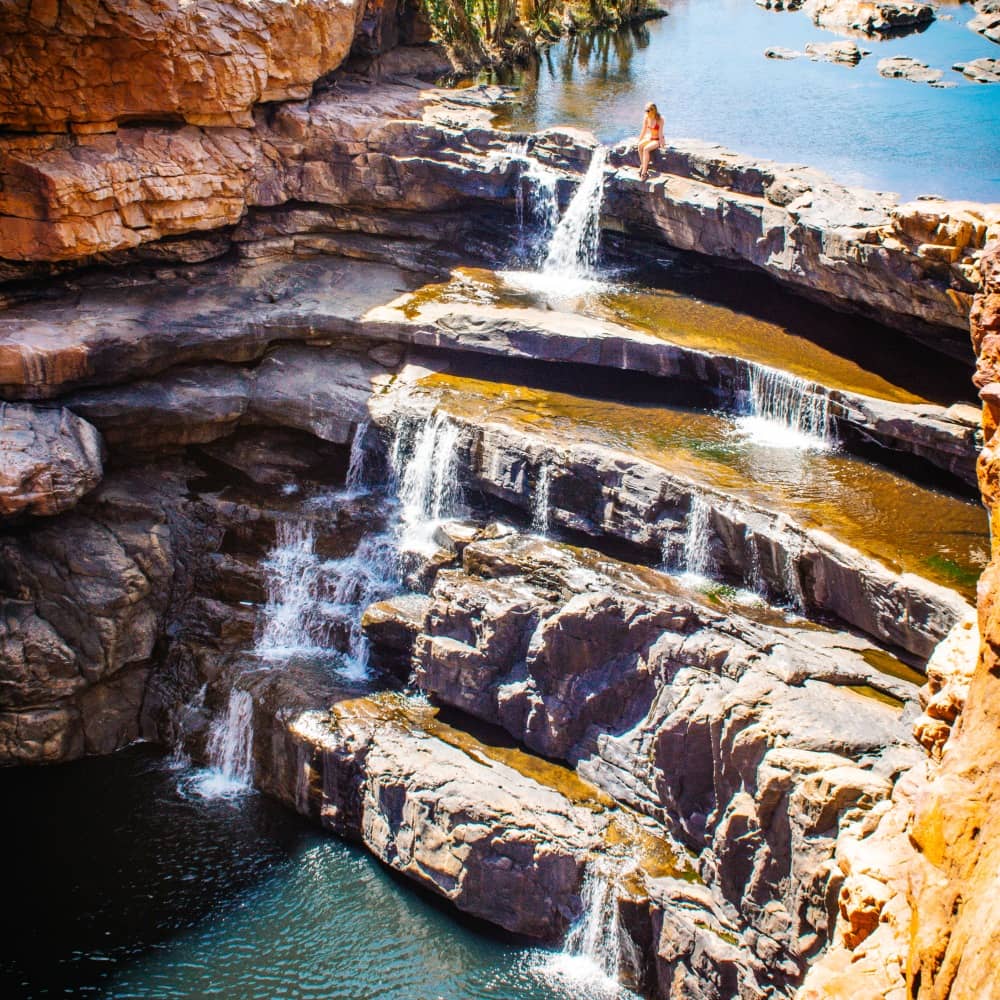 Young lady sitting on the waterfall of Bel Gorge. Also Known as Dalmanyi. In the King Leopold National Park close to Derny, Western Australia
