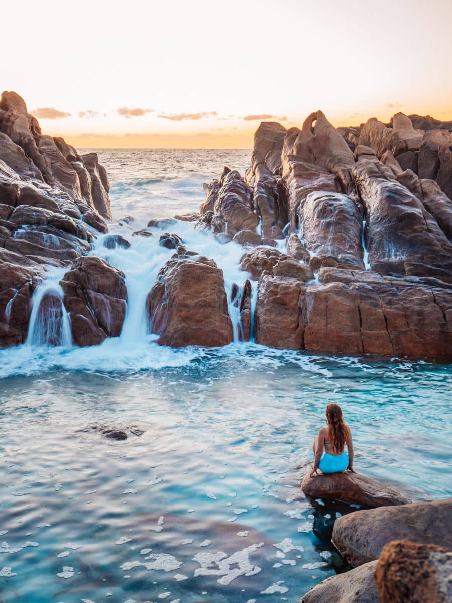 View of Bec sitting on a rock in front of Injidup Natural Spa at sunrise