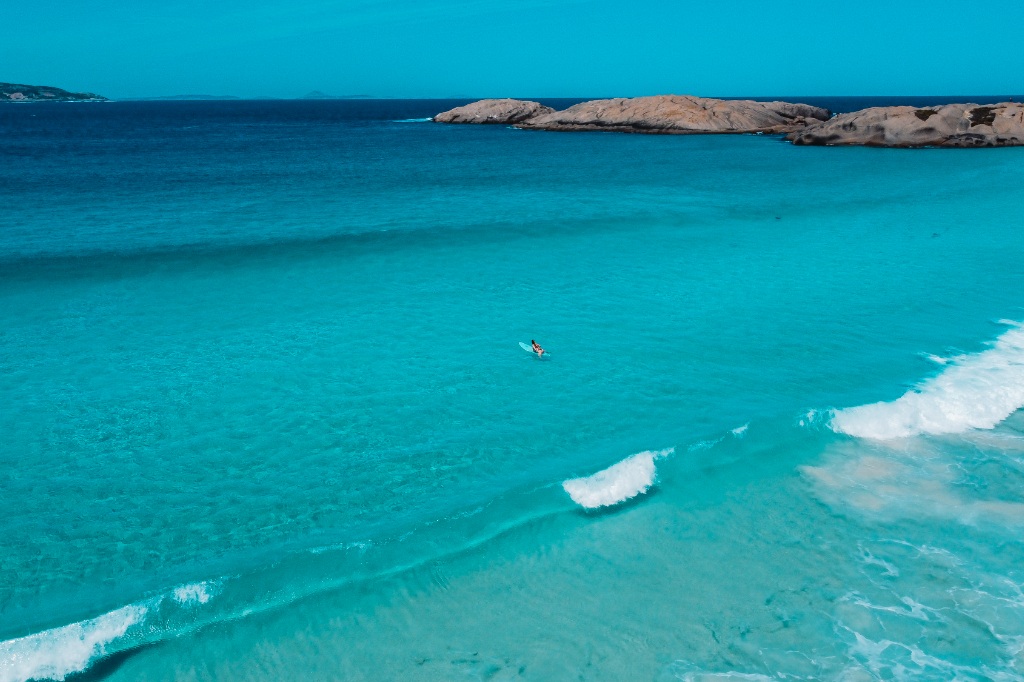 Woman surfing in Twilight Beach (Esperance, Western Australia) with turqouise waters and blue skies