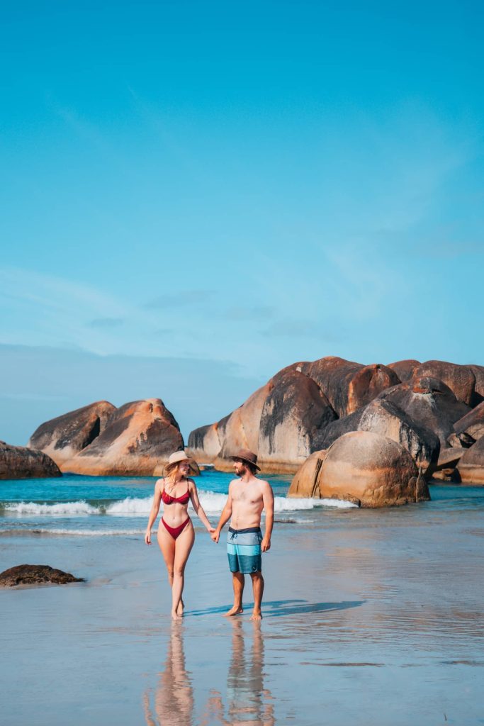 A happy couple enjoys a sunny day at a picturesque turquoise beach with rock formations at Denmark Western Australia