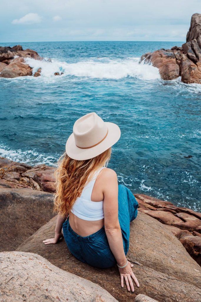 A woman sitting on a huge rock with beautiful scenic views of the sea at the Canal Rocks, Margaret River, Western Australia