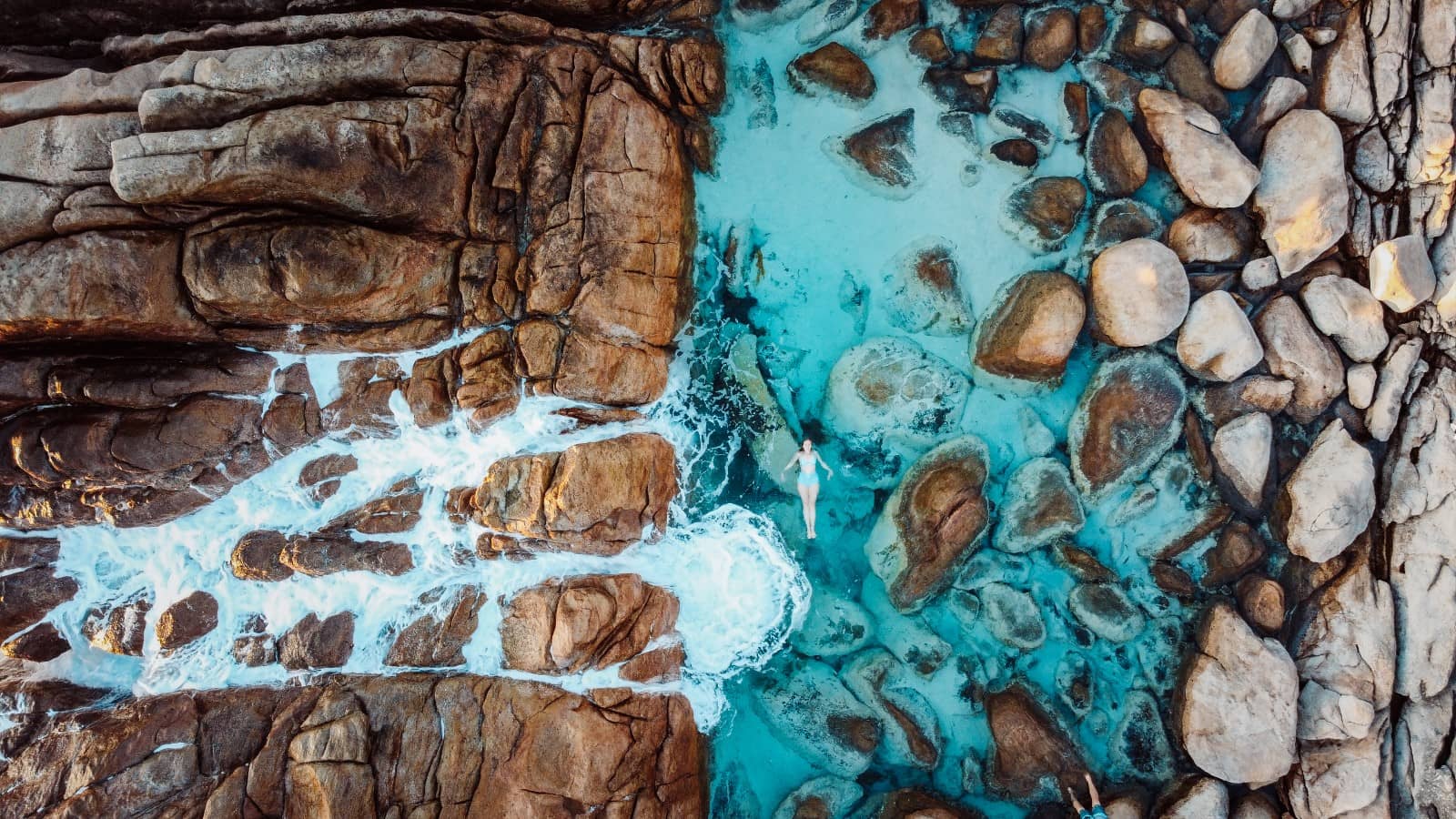 An aerial view of Injidup Natural Spa in Yallingup, Western Australia, showing a lone individual enjoying the serene, turquoise waters surrounded by the distinctive rock formations