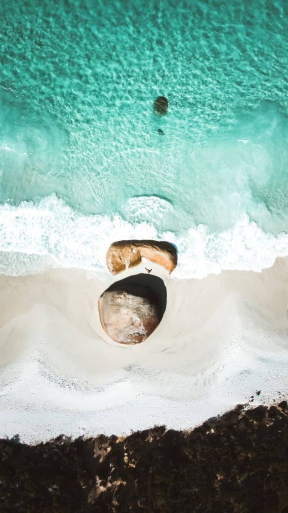 An aerial view of Little Beach in Albany, Western Australia, with the clear turquoise water of the ocean meeting the white sandy beach, and unique rock formations creating a natural cove.