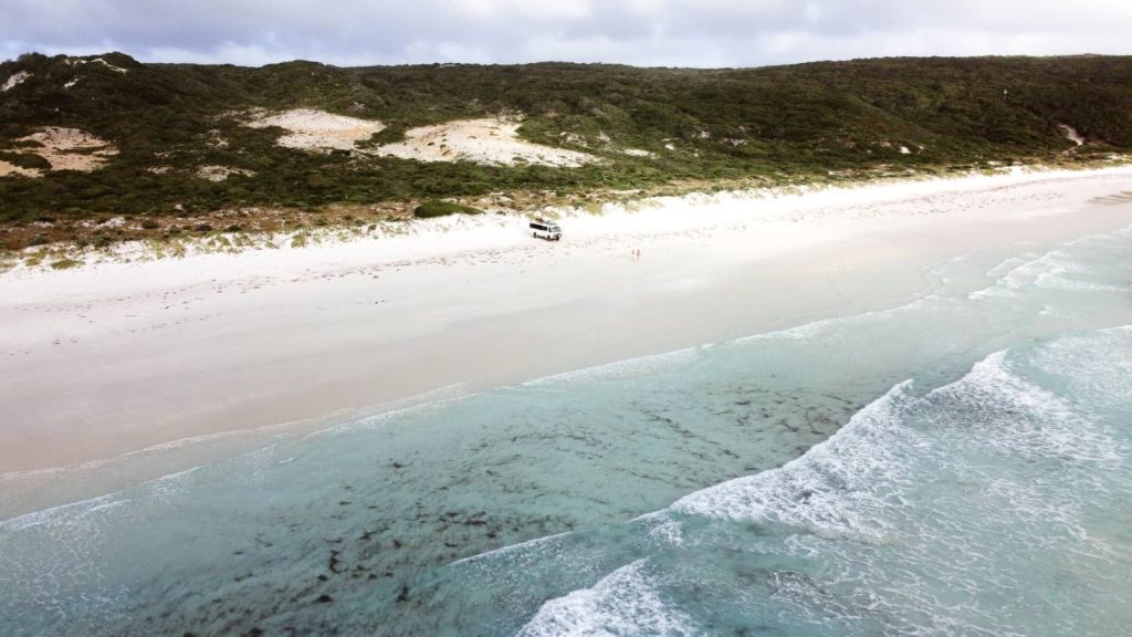 Aerial view of a beautiful beach in Bremer Bay Western Australia showing clear turquoise waters, white sandy shore, and one parked van surrounded by rugged dunes and lush greenery