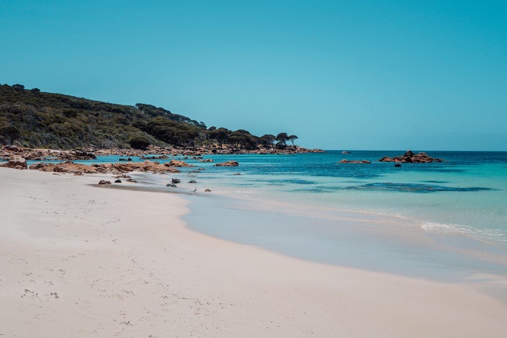 Serene beach scene at Bunker Bay, just minutes from Dunsborough, featuring pristine white sand, clear turquoise waters, and rocky outcrops along the shoreline under a clear blue sky. A must-visit for those seeking Things to do in Dunsborough.