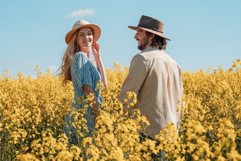 Chris and Bec standing in a field of yellow flowers under a clear blue sky. It shows the best time to visit Perth Western Australia