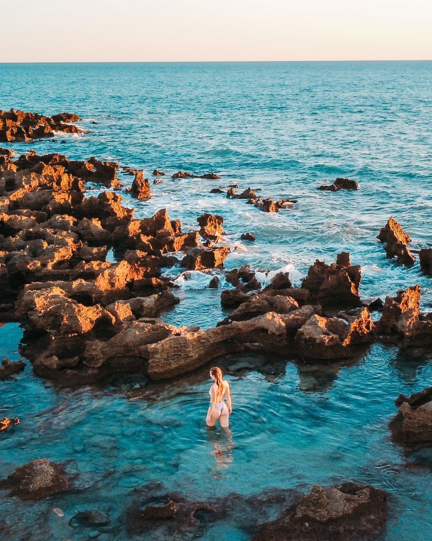 During sunset, a woman wades through the clear, shallow waters of the rock pools at Coconut Well in Broome, Western Australia. 