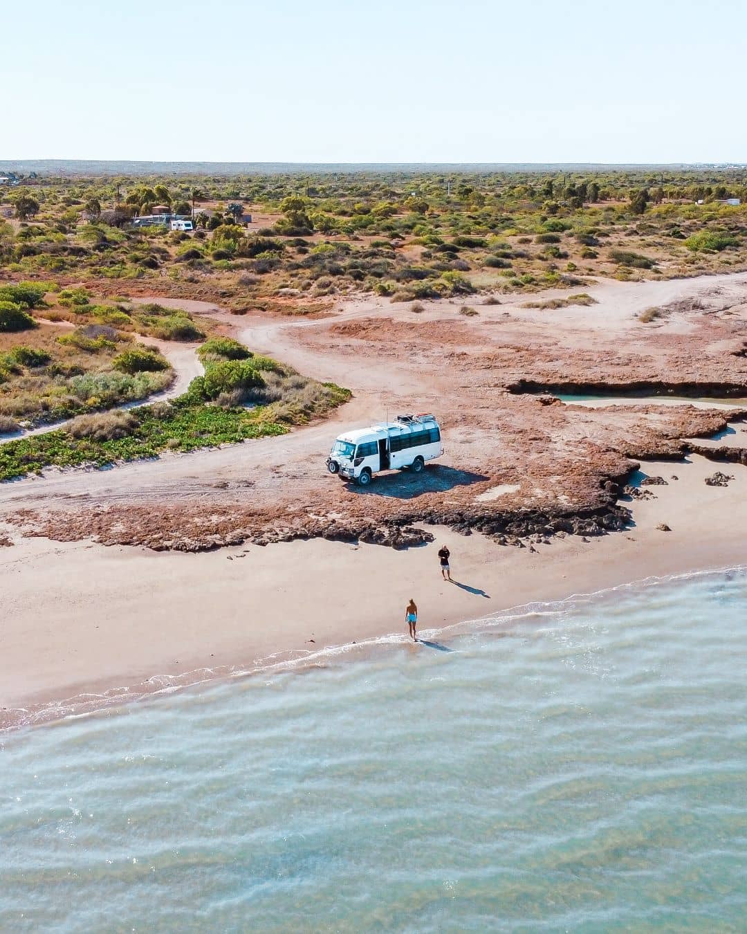 Aerial view of a white camper van parked on a beach in Cape Range National Park, with two people enjoying the scenic coastal environment.




