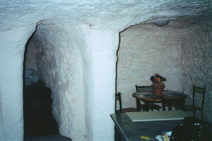 An underground room in Coober Pedy, South Australia, featuring a small dining table with chairs and a potted plant. The walls and ceiling are carved from the rock, highlighting the unique subterranean architecture of this opal mining town.