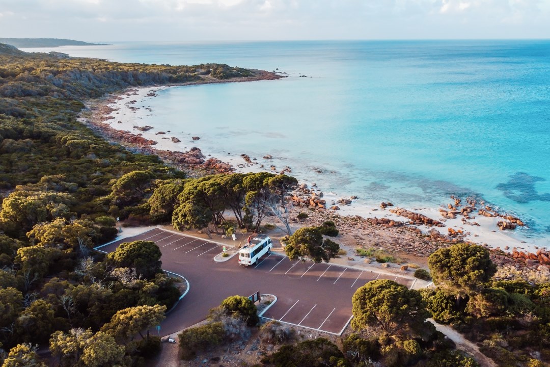 Aerial view of the Eagle Bay region in Dunsborough, Western Australia, showcasing a pristine coastline with turquoise waters, rocky shores, and dense greenery. A lone camper van is parked in an empty parking lot near the shoreline showing things to do in Dunsborough