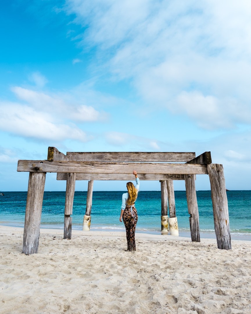 A woman stands under a wooden frame structure on the sandy shore of Hamelin Bay, Western Australia. This scene shows that Hamelin Bay is one of the best beaches in Margaret River region