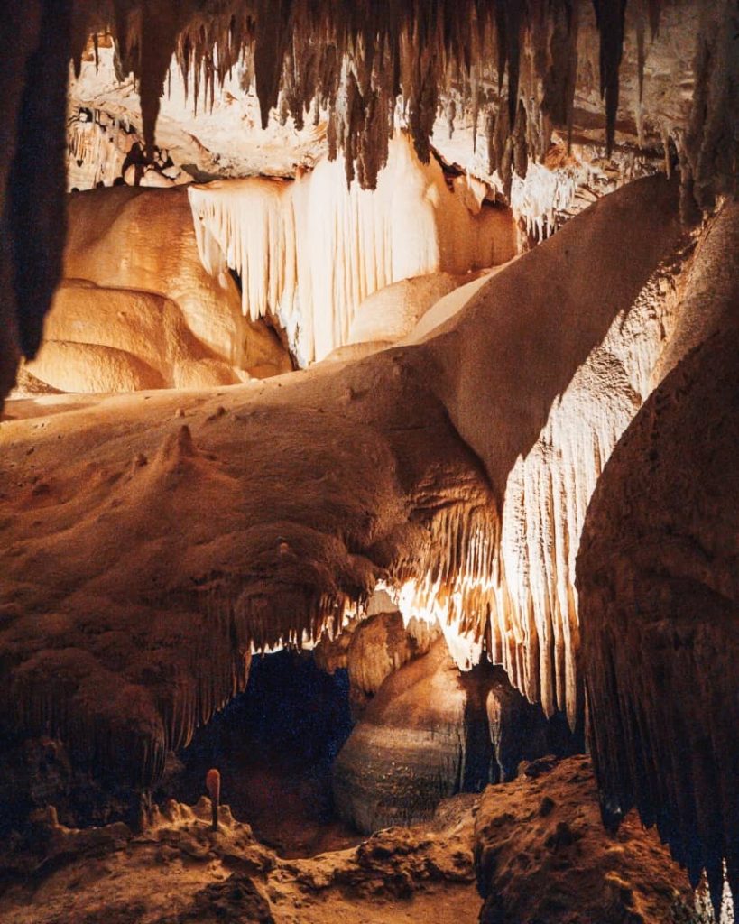 A view inside Jewel Cave showcases intricate and dramatic formations of stalactites and stalagmites. The lighting highlights the natural textures and shapes.