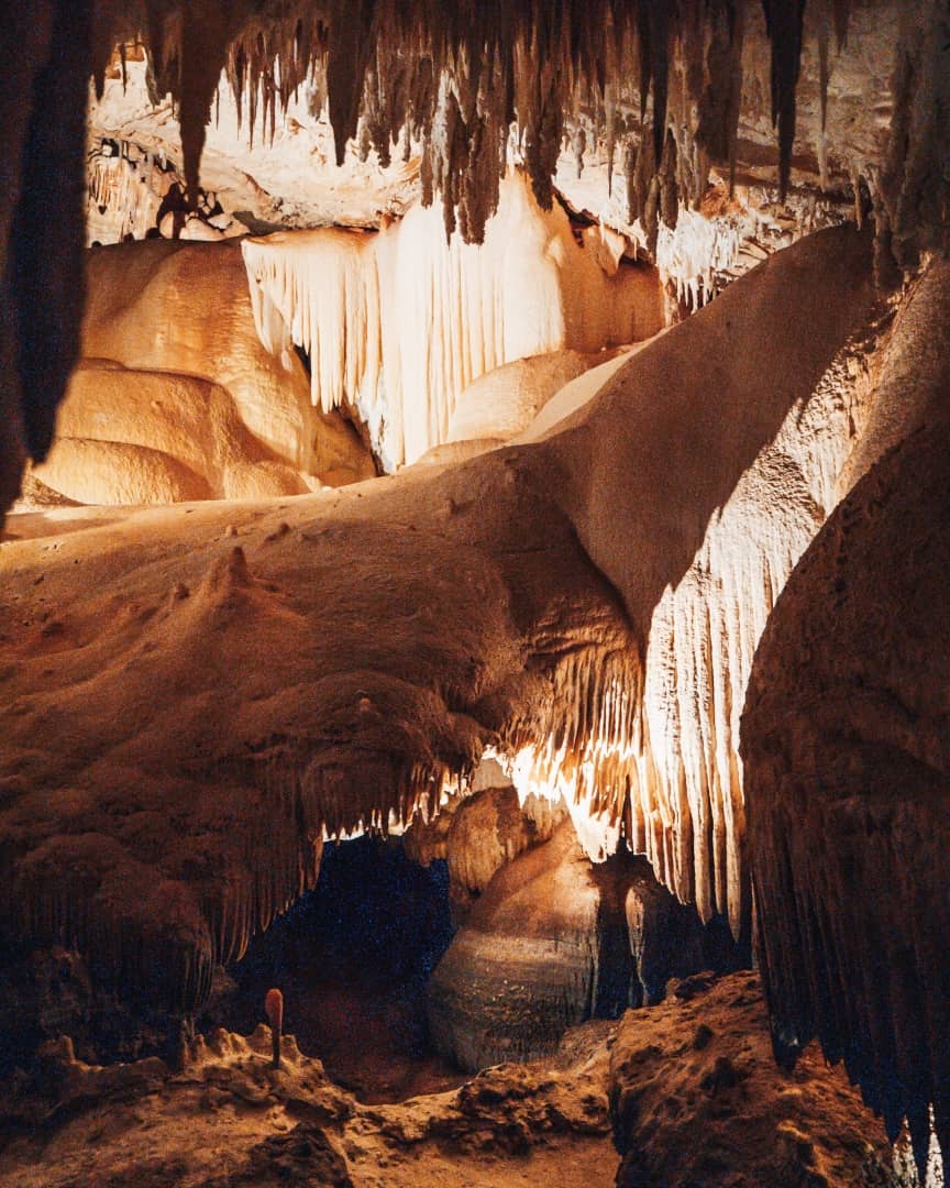 A view inside Jewel Cave showcases intricate and dramatic formations of stalactites and stalagmites. The lighting highlights the natural textures and shapes.