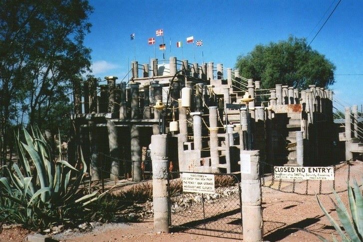The image shows Amigo’s Castle in Lightning Ridge, New South Wales, a unique stone structure adorned with various flags.
