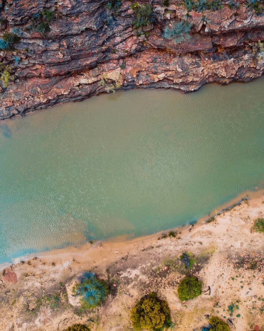 Aerial view of the Murchison River winding through the red rock formations and greenery of Kalbarri National Park. This scenic shot is a highlight for those interested in Kalbarri walks.