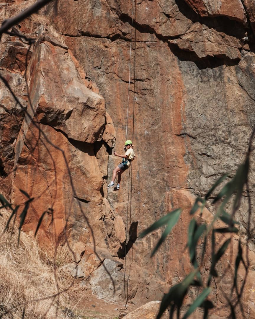 A person in a helmet and harness abseils down a rocky cliff face in Western Australia.
