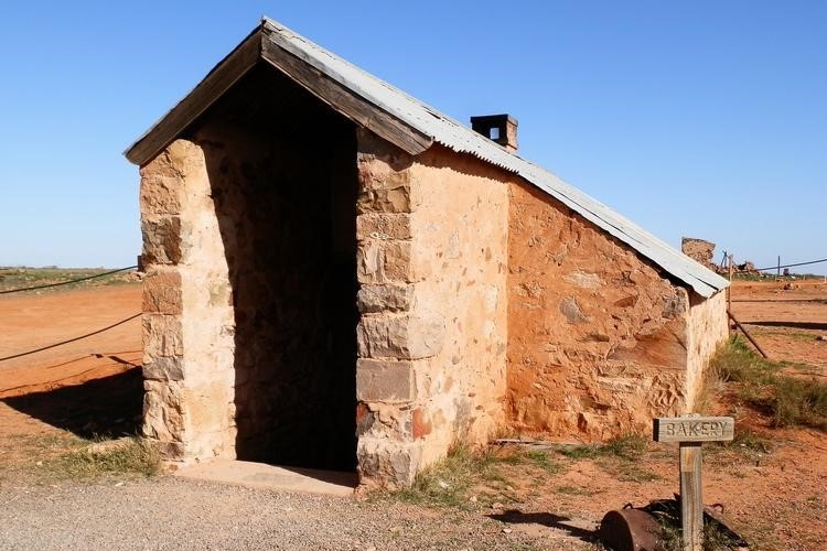 A small, rustic stone building with a metal roof, marked as the bakery in Farina, Outback South Australia. The structure has a simple sign that reads "Bakery" at its entrance.