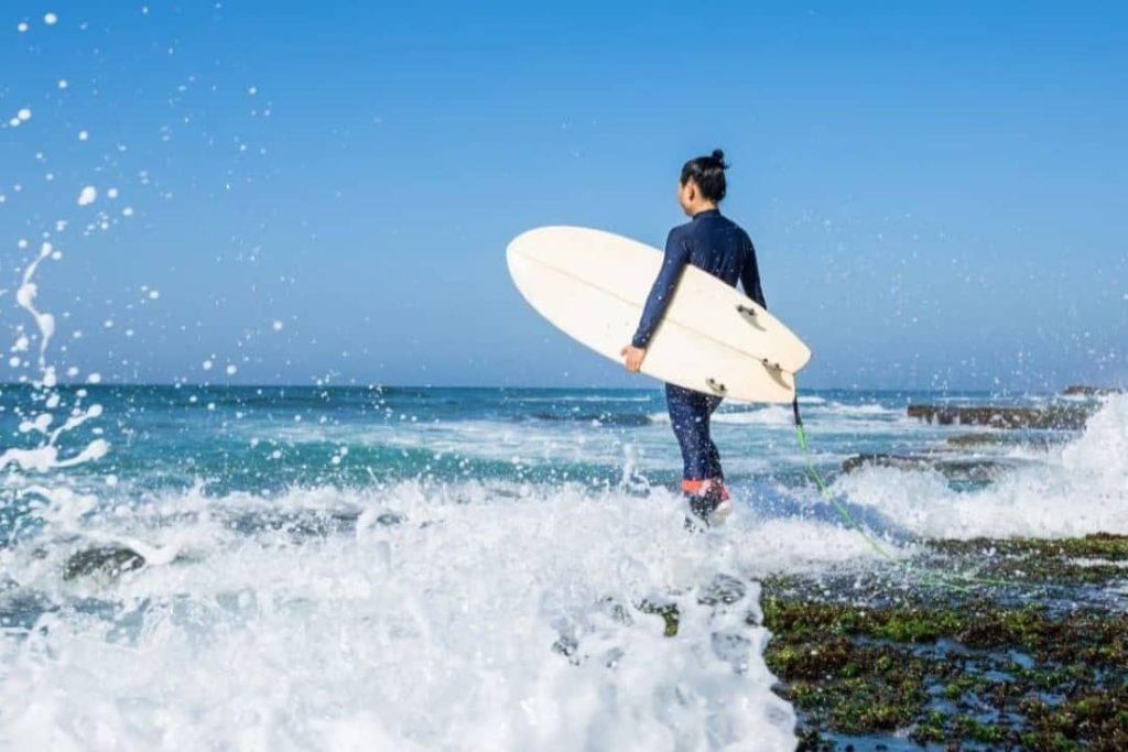 A woman carrying a surf board walking to the beach water