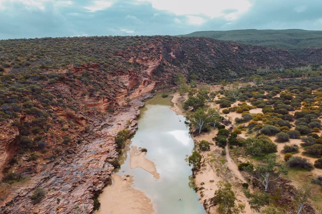Aerial view of the Loop Walk in Kalbarri National Park, Western Australia, featuring rugged red cliffs, sparse vegetation, and a winding river below.