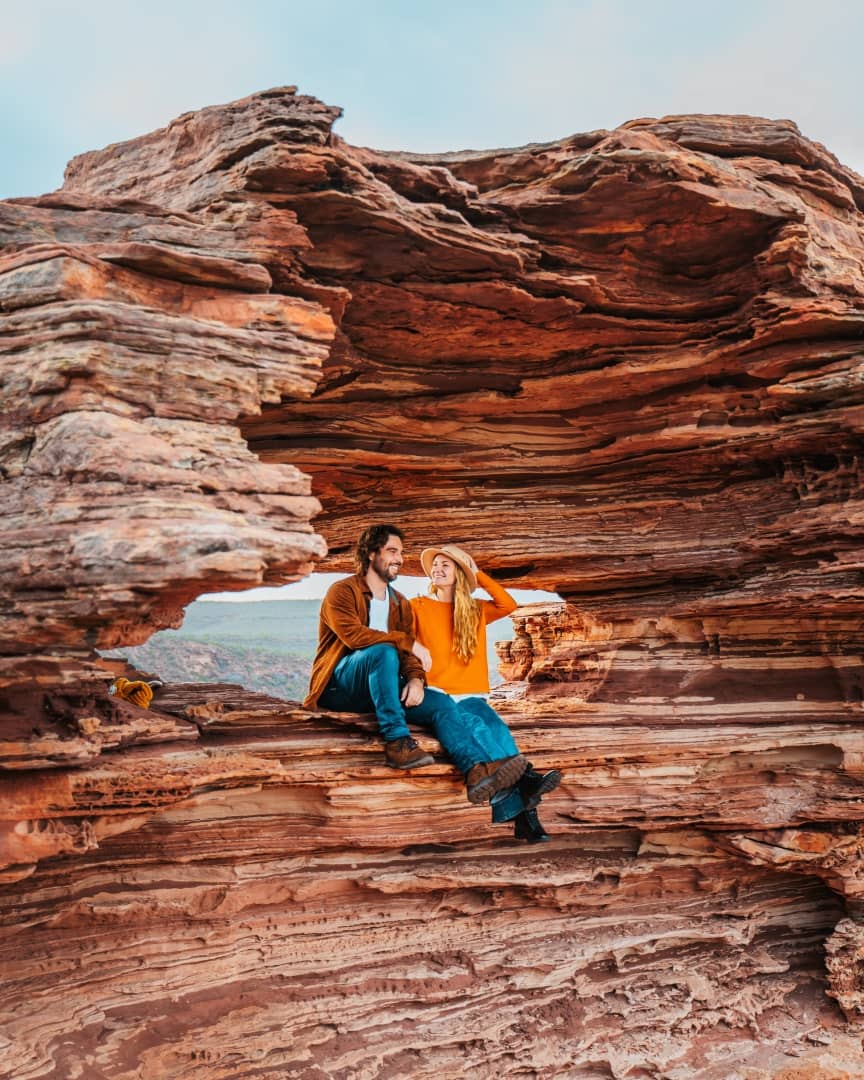 Two people sit at Nature's Window, a natural rock arch in Kalbarri National Park, Western Australia.