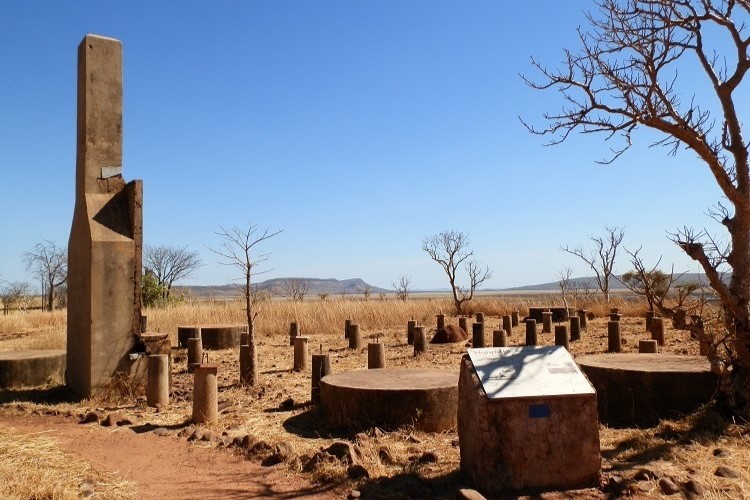 A dry, open landscape with scattered concrete pillars and a tall monument at Telegraph Hill in Parry’s Lagoon Nature Reserve. The scene includes sparse trees and distant hills under a bright, clear sky.