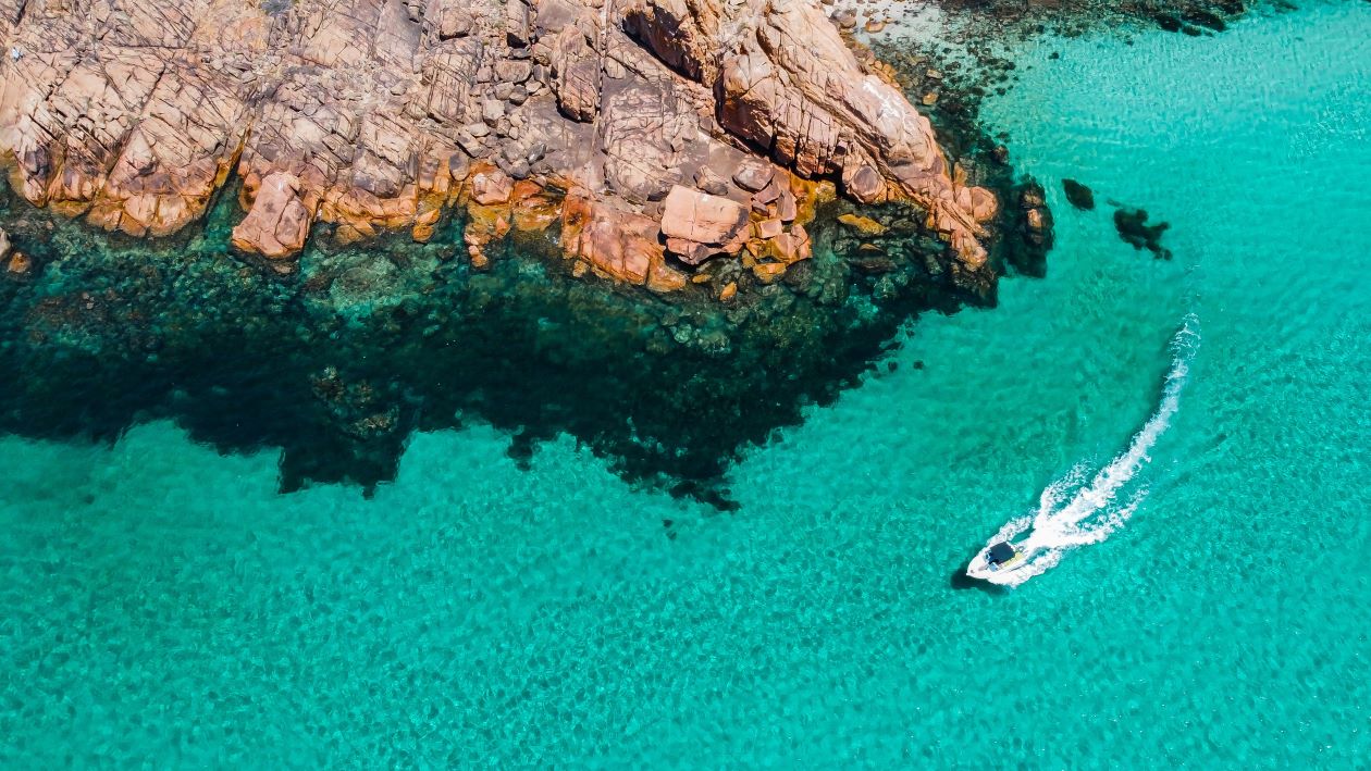A boat speeds across clear turquoise waters near rocky shores in Margaret River, Western Australia.
