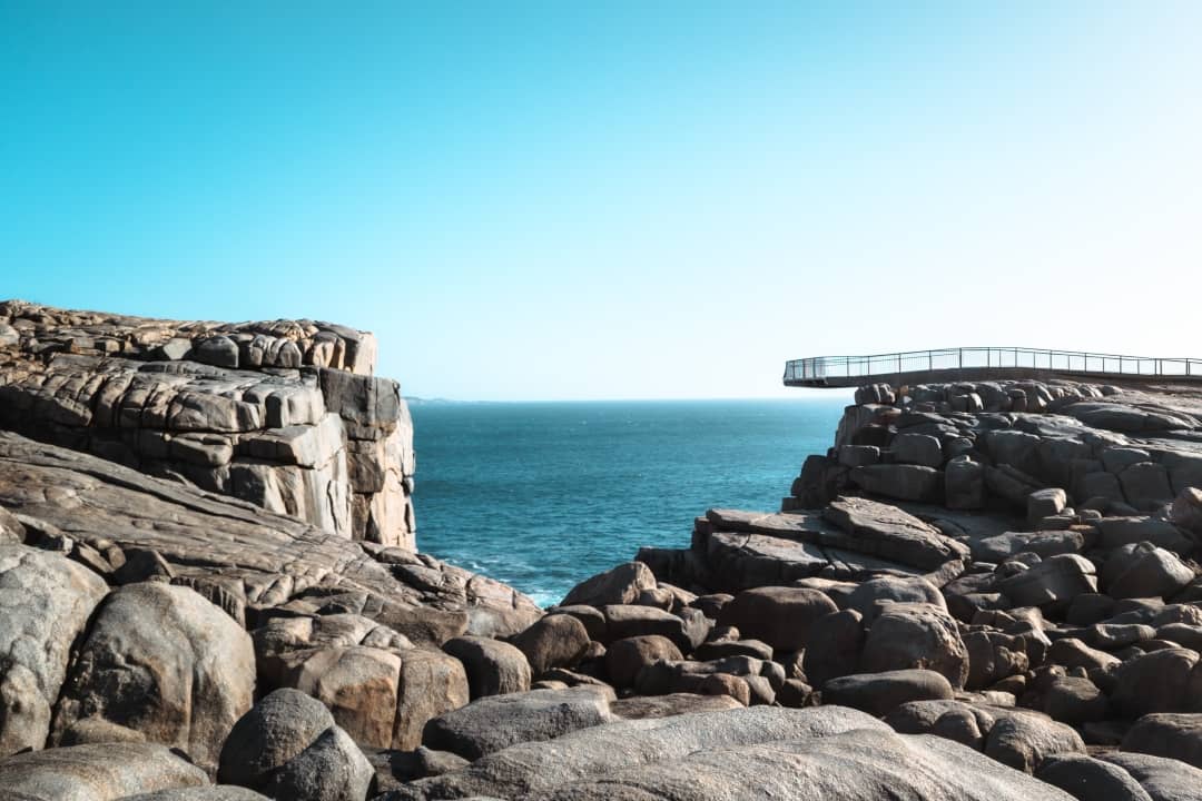 A panoramic view of The Gap in Albany, Western Australia, with a cantilevered platform extending over ancient rock formations above the blue ocean.