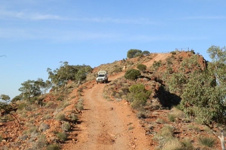 A 4WD vehicle navigating a steep descent from a lookout point, with panoramic views of the surrounding hills at Arkaroola Wilderness Sanctuary in South Australia.